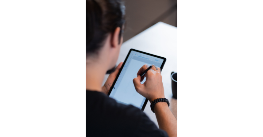 Person, die mit einem Stift auf einem Tablet-PC zeichnet, in einem Innenbereich.