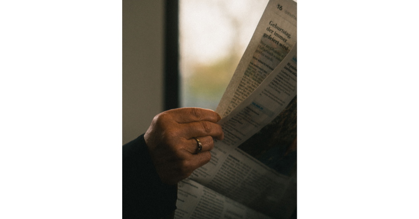 Eine Nahaufnahme einer Hand, die eine Zeitung drinnen hält und liest. - pexels, (c) Pascal Bronsert
